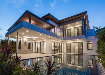 Modern two-story house with illuminated interior and exterior, featuring a swimming pool, at dusk.